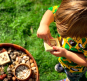 Child holding a Hellion Toys sustainable natural wooden vowel cube in a grass field