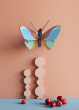 Studio Roof Claudina Butterfly decoration pictured on a peach coloured  painted wall, a few cherries are seen placed on a surface below 
