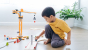Child kneeling on a wooden floor playing with the PlanToys crane with a wooden road set. 