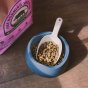 Beco Pets sustainably sourced bamboo pet food scoop in a bamboo bowl full of dog biscuits on a wooden floor.