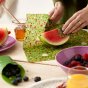 Close up of some hands wrapping a slice of watermelon in the land beeswax food wrap sheets from the Beeswax Wrap Co