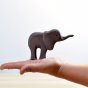 Hand holding the Bumbu eco-friendly hand carved small wooden elephant toy figure in front of a white background
