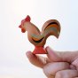 Close up of a hand holding the eco-friendly and plastic free wooden Bumbu Rooster toy on a white background