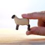 Close up of a hand holding the Bumbu childrens handmade miniature wooden running lamb toy on a white background
