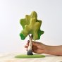Hand holding the Bumbu eco-friendly medium birch tree toy in green on a wooden table