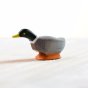 Close up of the Bumbu eco-friendly handmade wooden mallard duck toy leaning forwards on a wooden background