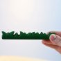 Close up of a hand holding the Bumbu plastic free wooden grass toy on a white background