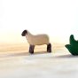 Bumbu kids small running lamb toy figure stood on a light wooden background next to a piece of bumbu wooden grass
