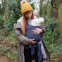 Woman stood in some woods wearing the Close caboo organic baby carrier in the blueberry blue colour