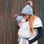Woman stood in front of a metal wall kissing a baby in the close caboo lite baby carrier in the blush colour