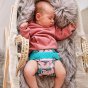 Sleeping baby wearing Pop-in light pink Ferret velcro Nappy all in one nappy with green trim details in a snuggly crib
