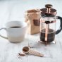 Eco living wooden coffee measure spoon on a grey wooden table next to a white mug of coffee 
