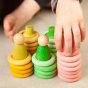 Grapat Summer Nins Seasonal Play Set, including nins, magos, mates, rings and coins in fresh spring colours of pink, green and yellow, stacked up and in play. Perfect for open-ended play. Close up of child's hand. 