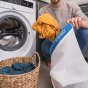 Man putting his dirty laundry into a Guppyfriend wash bag next to a white washing machine