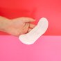 Hey Girls Natural Bamboo & Corn Fibre Disposable Panty Liners open in a persona hand on a red and pink background