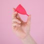 Hey Girls red Large Silicone Menstrual Cup held in someone's hand on a pink background