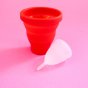 Hey Girls red Menstrual Cup Sterilising Pot with a small white menstrual cup on a pink background