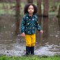 Girl stood in a large puddle wearing the dark blue little green radicals higher ground coat 