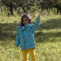 Girl stood in a green field holding a stick and wearing the LGR eco-friendly recycled plastic raincoat in the leo lion blue colour