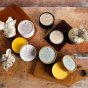 Oakdale Bees natural beeswax Beevitalise wood remedy, leather revive and board and bowl restore balm on a wooden floor next to a wooden chopping board and leather wallet