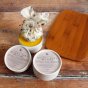 Two tubs of Oakdale Bees Beevitalise natural beeswax wooden board and bowl balm on a wooden floor next to a wooden chopping board