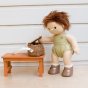 Olli Ella dinkum doll stood next to a small wooden table opening its rattan dollychari backpack