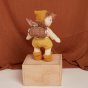 Olli ella dinkum doll stood on a wooden box wearing a rattan dollychari backpack in front of a brown sheet background