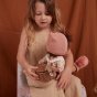 Olli ella dinkum doll sat backwards on a girls knee wearing the rattan dollychari natural wooden backpack