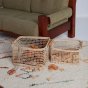 2 natural woven olli ella cabouche rattan baskets filled with wooden toys on a white carpet next to a green, wooden sofa