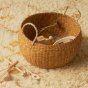 Olli Ella eco-friendly woven display basket in the clay and mustard colour on a fluffy carpet, filled with toys