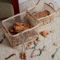 2 natural woven olli ella cabouche rattan baskets filled with wooden toys on a white carpet