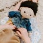 Close up of a childs hands dressing an Olli Ella dinkum doll in the sage travel togs outfit set