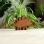 O-WOW sustainably sourced walnut stegosaurus dinosaur toy on a wooden work top in front of a green house plant