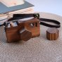 O-WOW handmade wooden camera toy on a woven placemat on a white table next to a close book