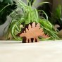 O-WOW sustainably sourced walnut stegosaurus dinosaur toy on a wooden work top in front of a green house plant