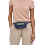 Close up of woman wearing the Patagonia black hole mini bum bag in current blue around her waist on a white background