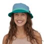 Woman stood on a white background wearing the lago blue wavefarer bucket sun hat