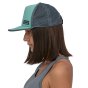Woman stood sideways on a white background wearing the Patagonia eco-friendly teal blue duckbill trucker cap 