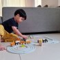 Boy sat on the floor playing with the plan toys plastic free wooden trains on the plan world rubber train track