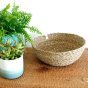Large respiin woven seagrass bowl on a tan placeman in front of a white wall next to a plant
