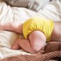 Close up of a baby wearing the Tots Bots eco-friendly reusable bamboozle stretch nappy in the catkin colour on a white bed