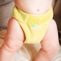 Baby stood on a white bed wearing the Tots Bots eco-friendly bamboozle stretch baby nappy in the catkin colour