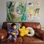Young boy sat on the sofa with the Wonder Cloths large jungle and world map play cloths hung up on the wall behind