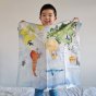 Young boy stood on a bed holding up a large Wonder Cloth in the world map print