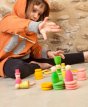 Grapat Summer Nins Seasonal Play Set, including nins, magos, mates, rings and coins in fresh spring colours of pink, green and yellow, stacked up and in play. Perfect for open-ended play. Child playing in front of stone wall. 