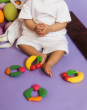 A toddler sits with four Oli & Carol 100% Natural Rubber Baby Teething Rings at their feet