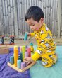 Young boy playing outside with some wooden blocks wearing the DUNS Sweden organic cotton zip suit in the yellow puffin print
