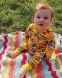 Young boy sat on a blanket on some grass wearing the DUNS Sweden organic cotton zip suit in the lemon chrome puffin print