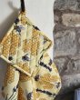 DUNS Sweden organic cotton linen pot holder and tea towel in the bee yellow print hanging from a metal hook in front of a stone wall 