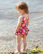 Young girl stood backwards by the sea wearing the Frugi flower power nappy swimsuit